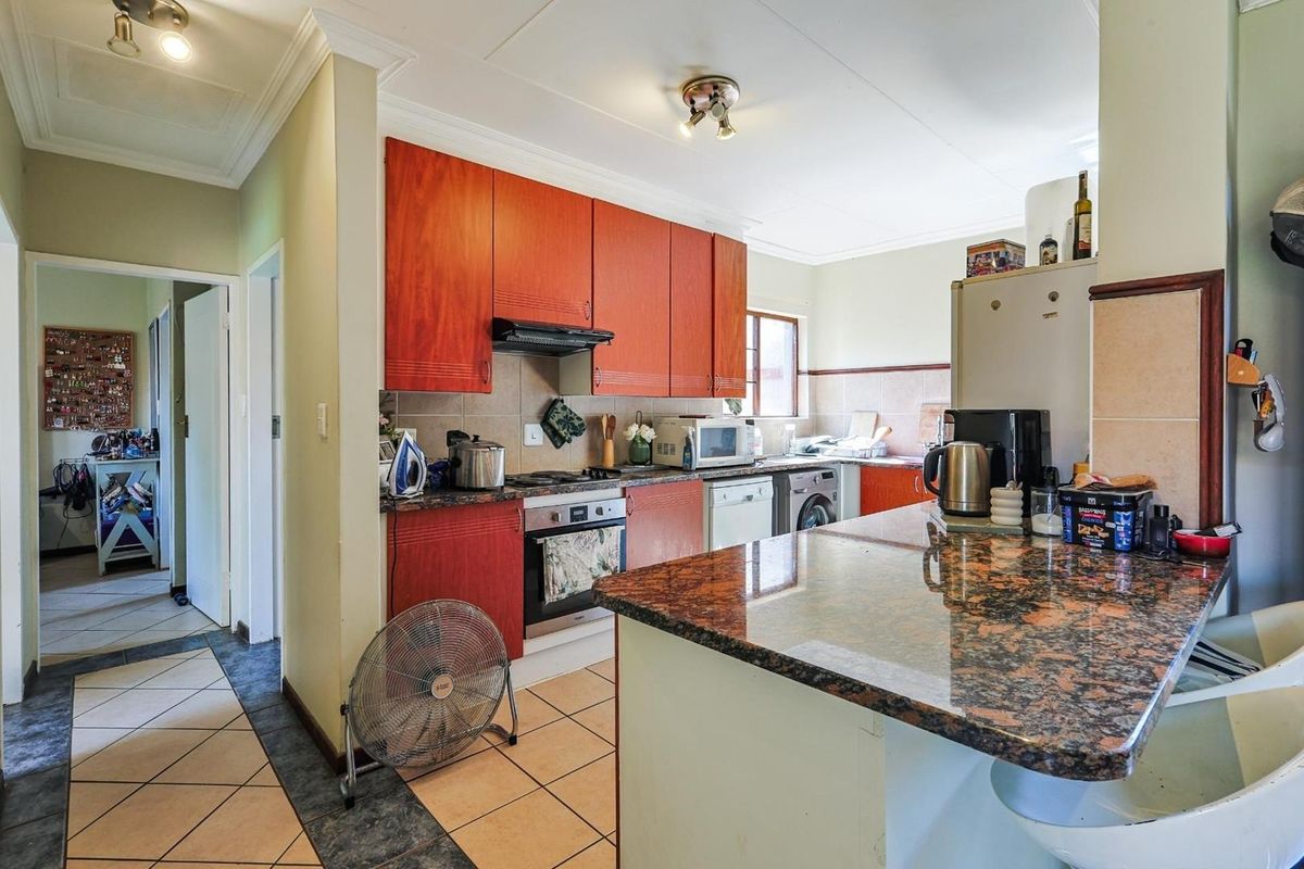 A functional kitchen featuring wood-toned cabinetry, granite-style countertops, a built-in oven, and a breakfast bar, with an adjacent tiled hallway.
