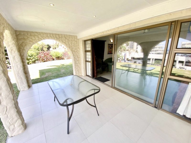 A covered patio featuring distinctive stone-clad arches, tiled flooring, and large sliding glass doors providing seamless access to the interior living space.