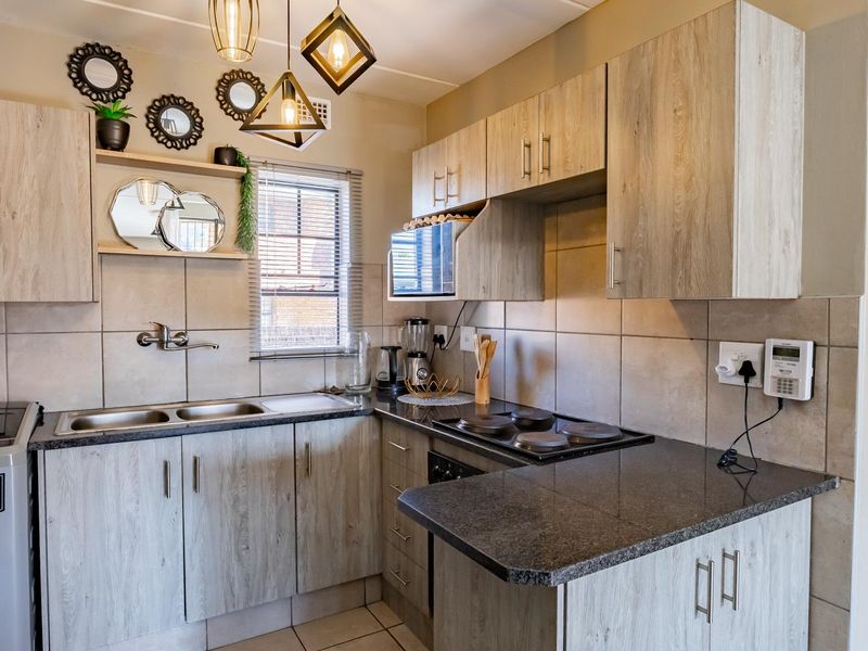 A well-maintained kitchen featuring light wood-look laminate cabinetry, dark granite countertops, a double basin sink, and a built-in electric hob and oven.