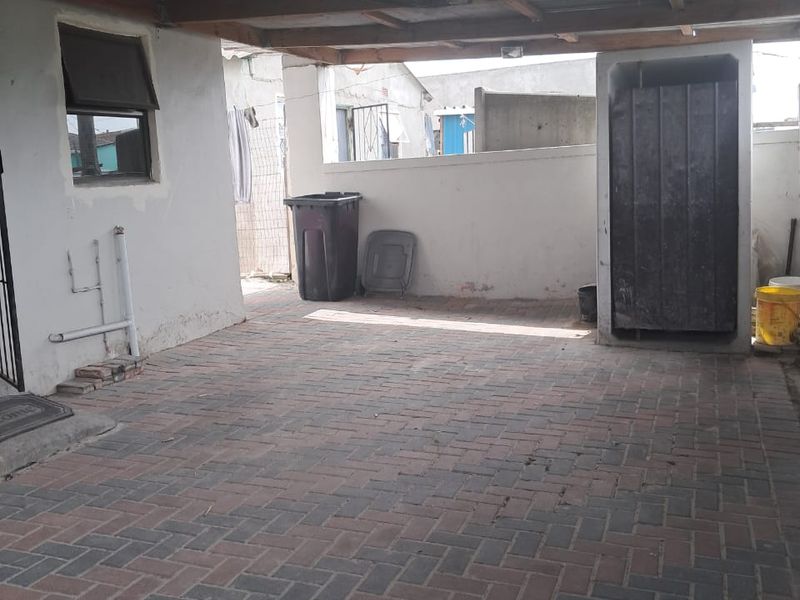 A covered outdoor patio area featuring paved flooring and a timber-framed roof structure, providing a functional space for outdoor utility or entertainment.