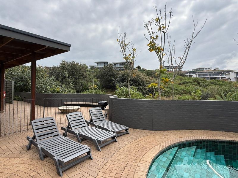 Outdoor pool area featuring a tiled swimming pool, paved surround, covered patio section, and a low retaining wall with views of the surrounding landscape.