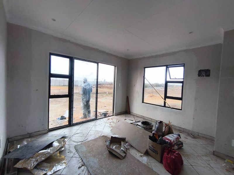 An unfinished living room space featuring tiled floors, aluminium window frames, and sliding doors, currently undergoing construction and plastering work.
