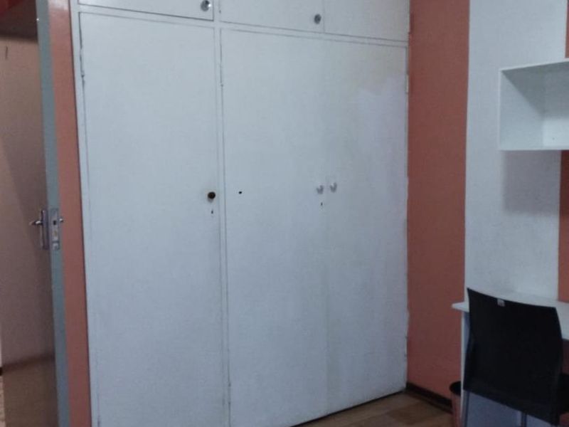 A bedroom featuring built-in cupboards with overhead storage and laminate flooring, providing functional storage space.
