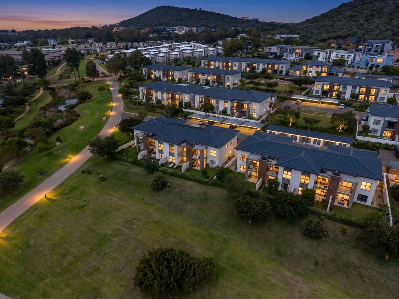 Aerial view of a modern apartment complex at dusk, featuring well-maintained landscaping, paved pathways, and integrated covered parking facilities.