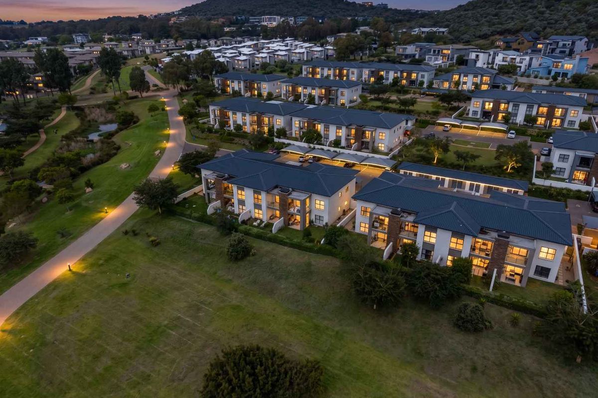 Aerial view of a modern apartment complex at dusk, featuring well-maintained landscaping, paved pathways, and integrated covered parking facilities.