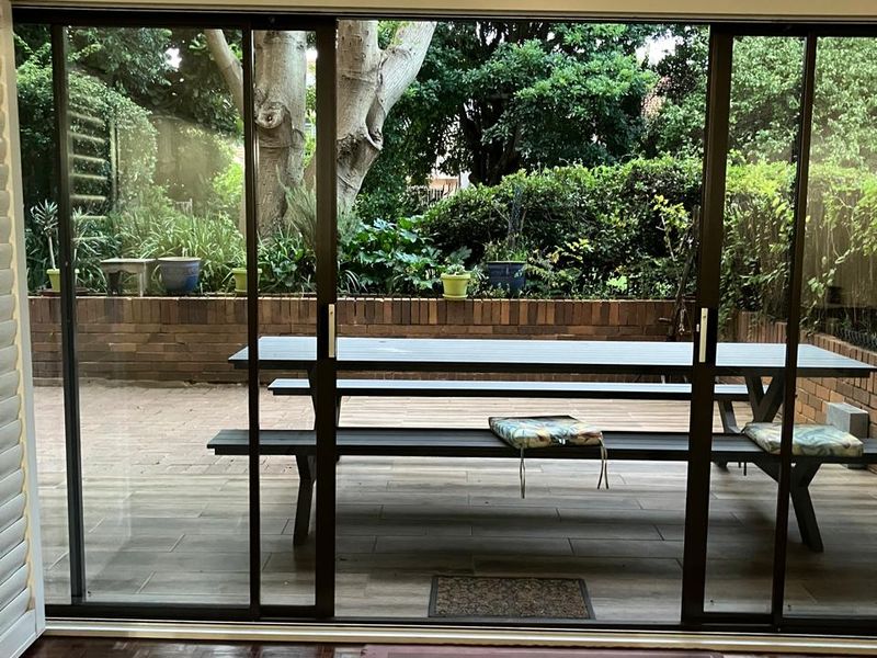 Living room featuring large sliding glass doors that open onto a tiled patio and garden area with a brick retaining wall.