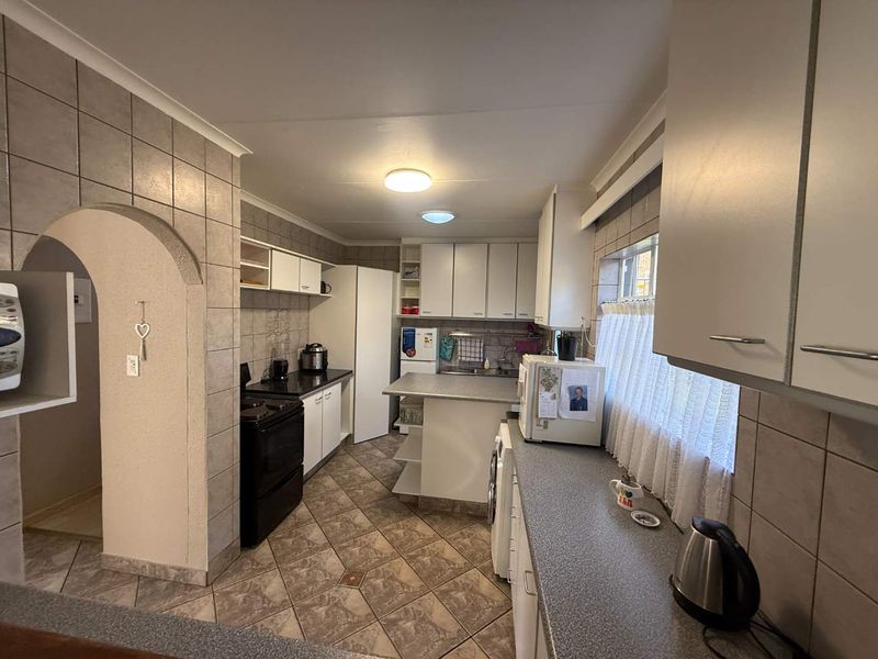 A functional kitchen featuring tiled flooring, ample built-in cabinetry, laminate countertops, and a distinctive arched entryway leading to adjacent living spaces.