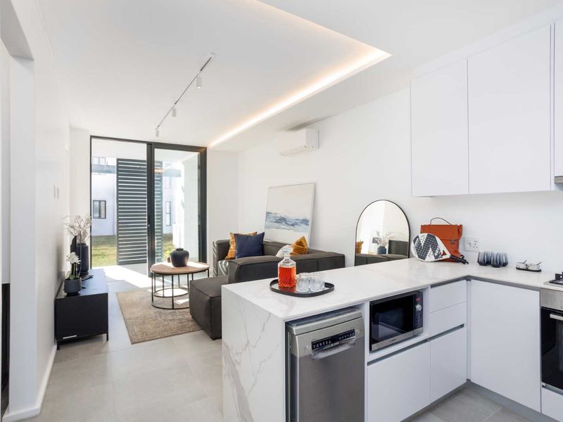 Modern open-plan living area featuring a sleek kitchen with stone countertops, integrated appliances, recessed lighting, and seamless access to the outdoor space.