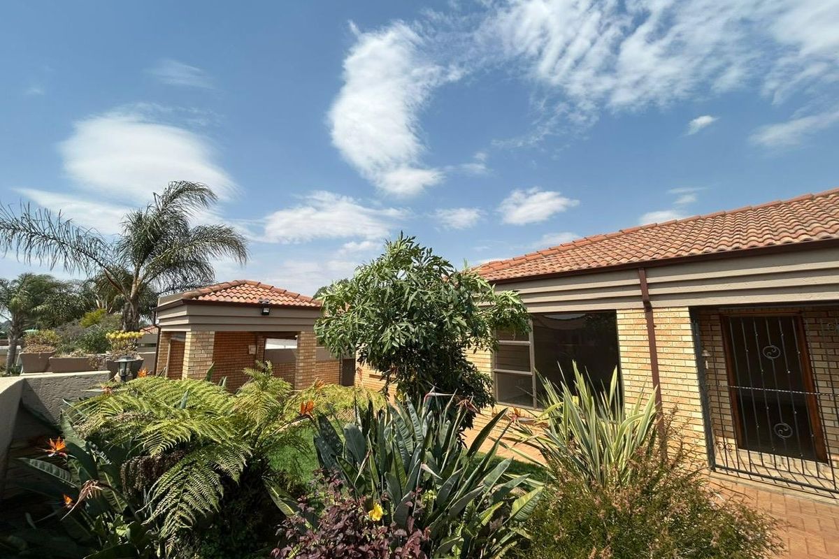 A well-maintained rear exterior view of the cluster home featuring a facebrick facade, terracotta roof tiles, and a paved patio area with established garden.