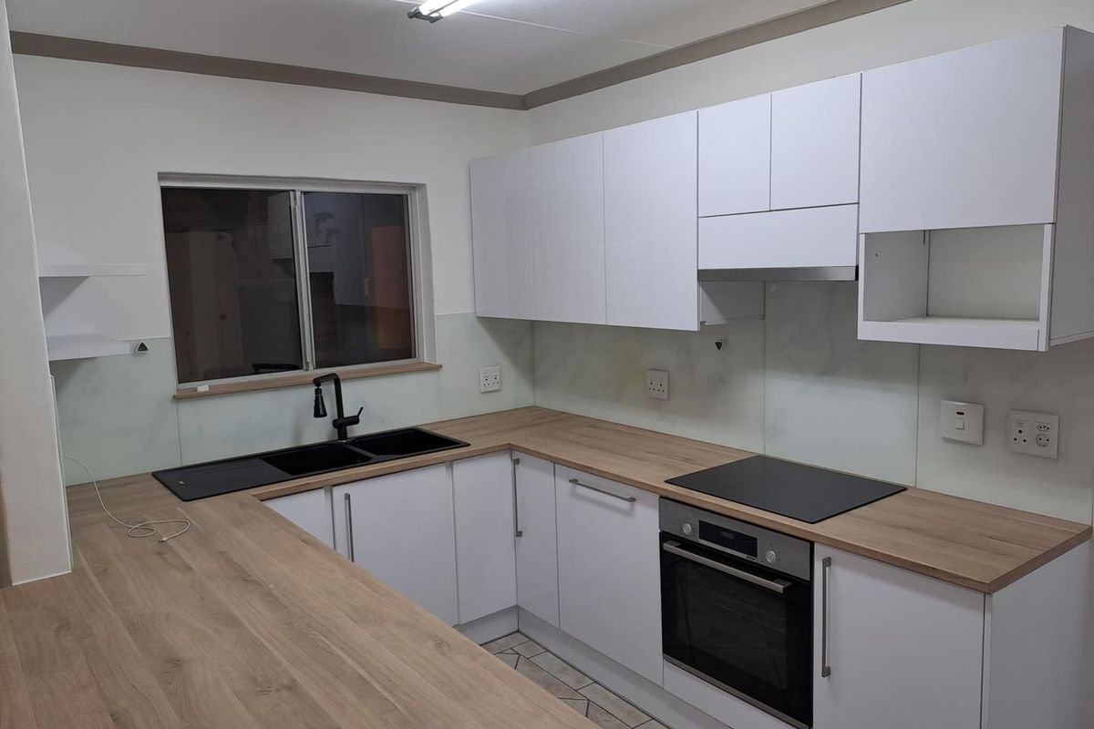 Modern kitchen featuring white cabinetry, wood-look laminate countertops, integrated oven, electric hob, and a double sink with a contemporary black tap.