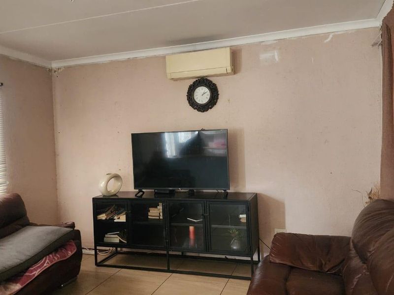 A living room featuring tiled flooring and a wall-mounted split-system air conditioner, currently showing signs of wear on the wall surfaces.