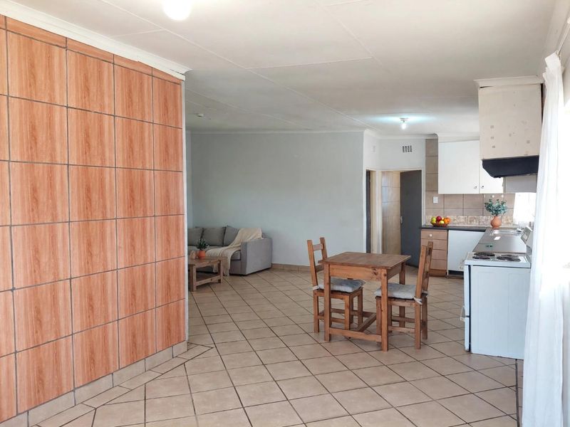 Open-plan living and kitchen area featuring tiled flooring, dated wall finishes, and functional built-in cabinetry with an integrated extractor fan.