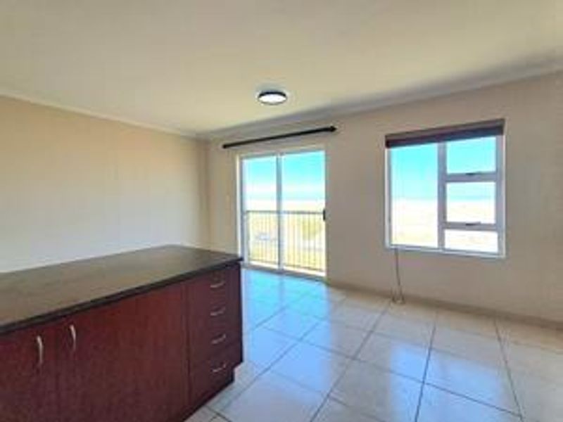 An open-plan living area featuring tiled flooring, built-in cabinetry, and large windows providing natural light and access to a balcony.