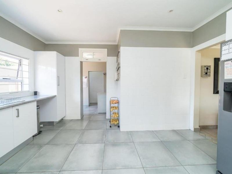 A functional kitchen featuring tiled flooring, white cabinetry, and a tiled splashback, offering a clean and practical workspace with direct access to adjacent areas.