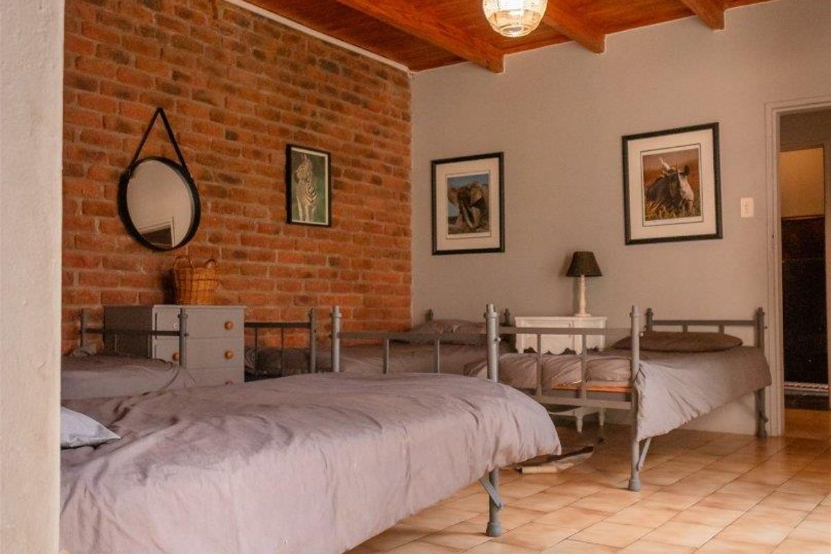 A spacious bedroom featuring a rustic exposed brick feature wall, high timber-beamed ceilings, and durable tiled flooring.
