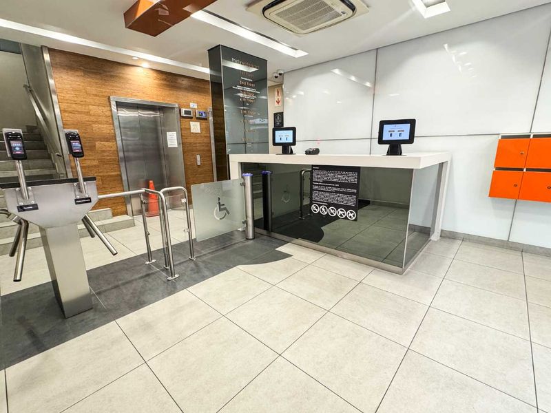 Modern office building lobby featuring a reception desk, secure turnstile access control, elevator access, and professional tiled finishes.