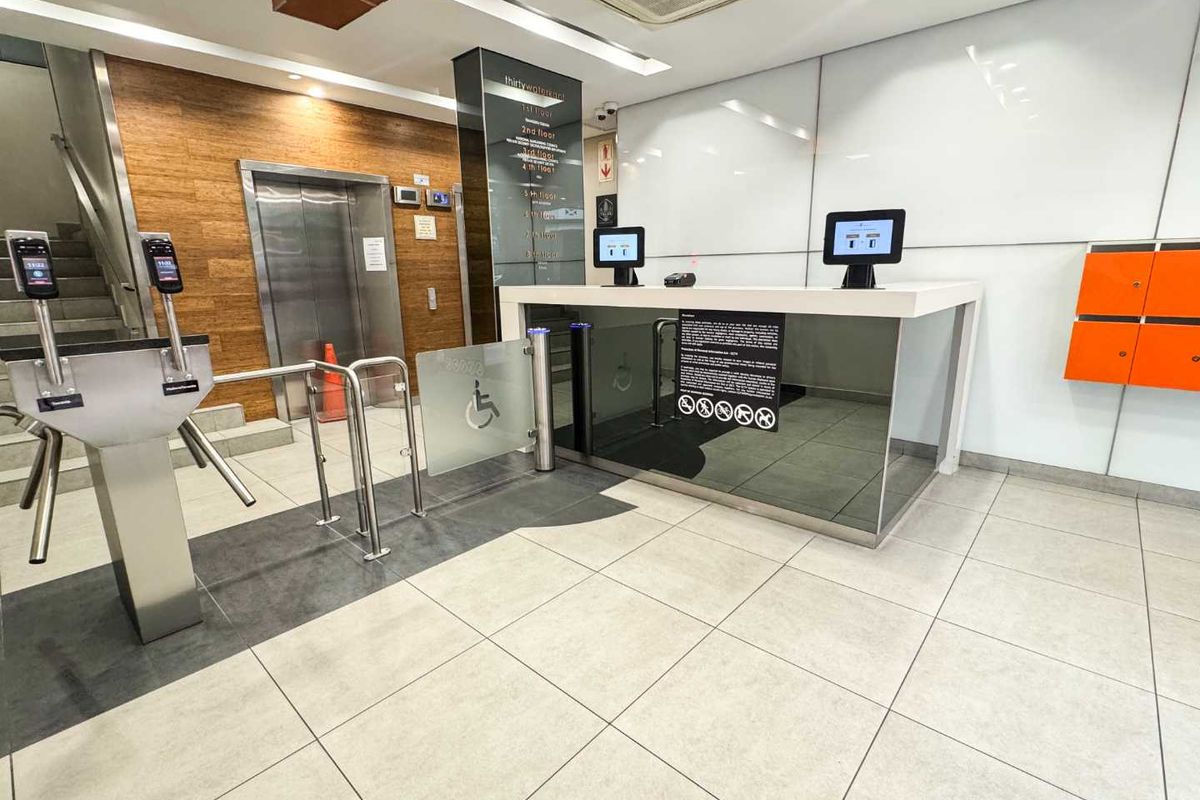 Modern office building lobby featuring a reception desk, secure turnstile access control, elevator access, and professional tiled finishes.