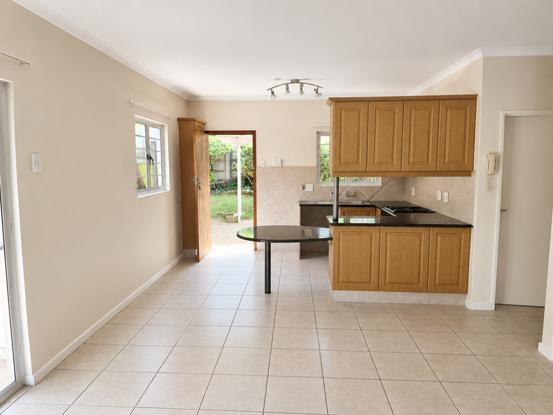 Open-plan kitchen and living area featuring tiled flooring, wooden cabinetry, granite countertops, and direct access to the rear garden.
