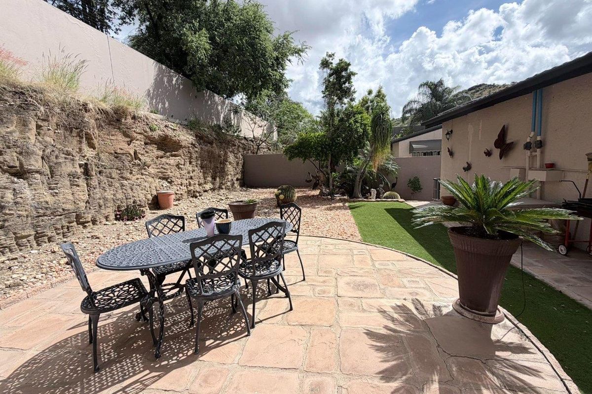 A rear garden area featuring a stone-paved patio, artificial lawn section, and a natural rock retaining wall boundary.