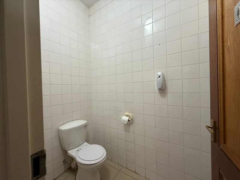 A functional commercial restroom featuring full-height white ceramic wall tiling, tiled flooring, and standard sanitary fixtures.
