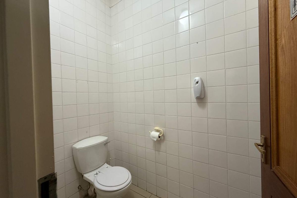 A functional commercial restroom featuring full-height white ceramic wall tiling, tiled flooring, and standard sanitary fixtures.