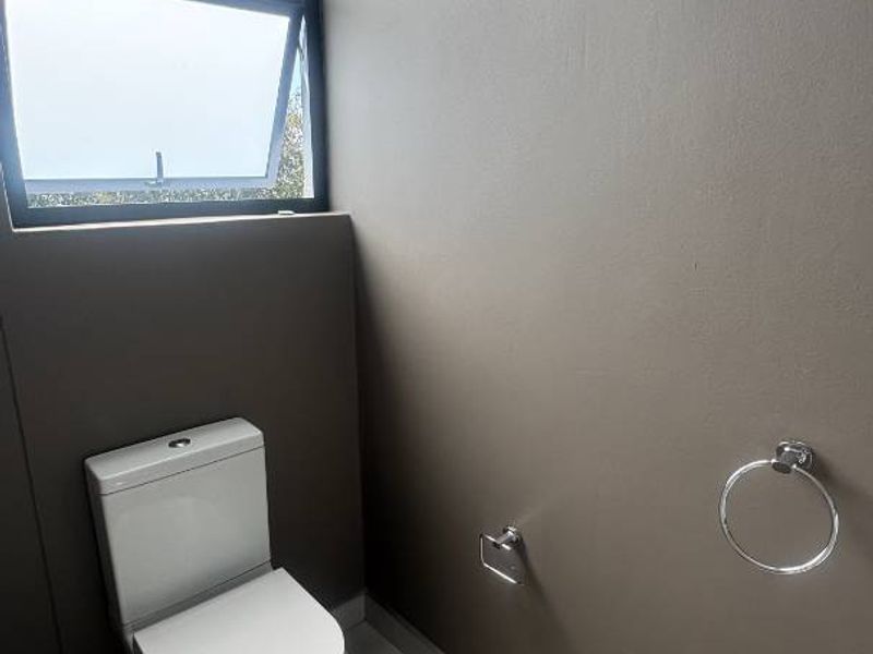 A clean and modern guest bathroom featuring neutral wall tones, large format floor tiles, and a functional top-hung window for natural ventilation.