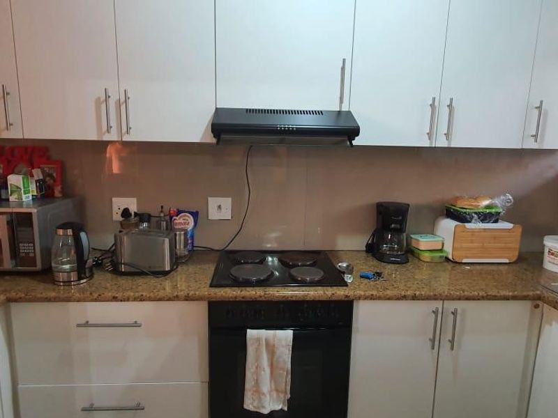 A functional kitchen featuring white cabinetry, granite countertops, a built-in oven with an electric hob, and an integrated extractor fan.
