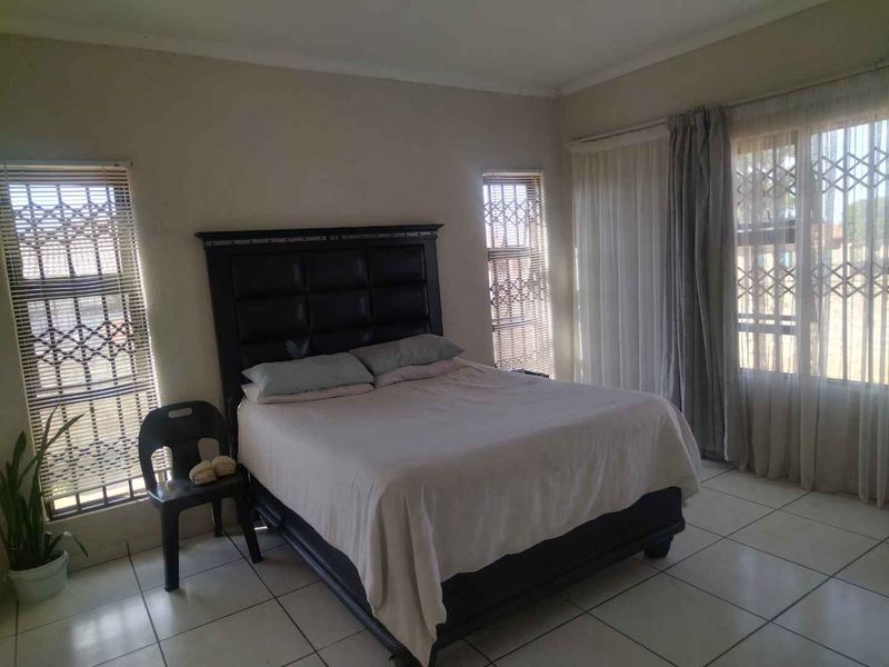 A spacious bedroom featuring tiled flooring and large windows fitted with security bars and curtain tracks.
