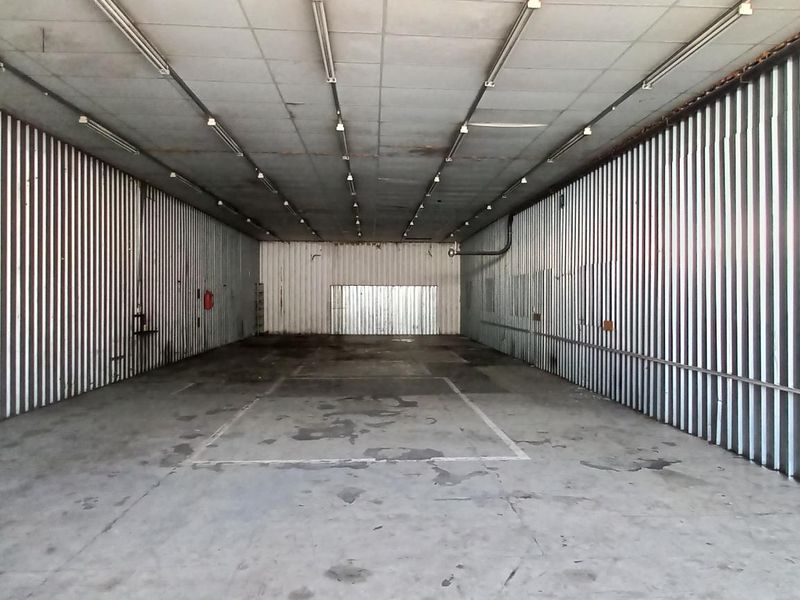 A large, empty industrial garage space featuring corrugated metal walls, concrete flooring, and overhead fluorescent lighting, suitable for storage or workshop use.