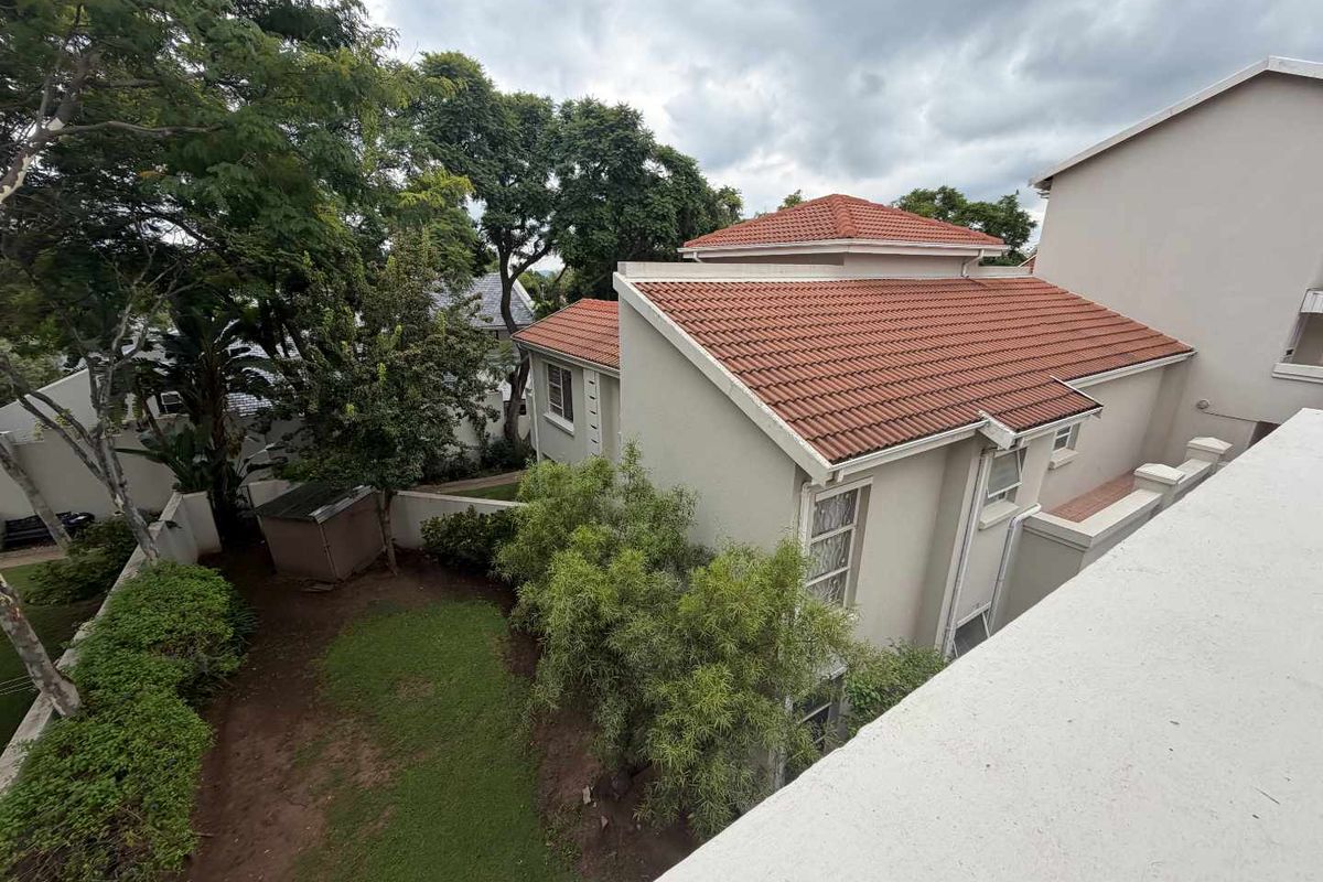 An elevated view of the property's rear exterior, featuring a tiled roof, landscaped garden area, and perimeter boundary walls.