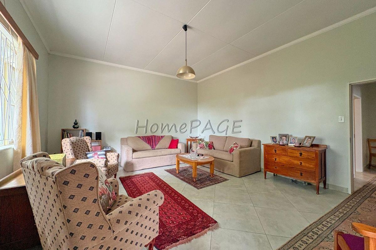 A spacious living room featuring tiled flooring, a central pendant light fixture, and large windows with security bars.