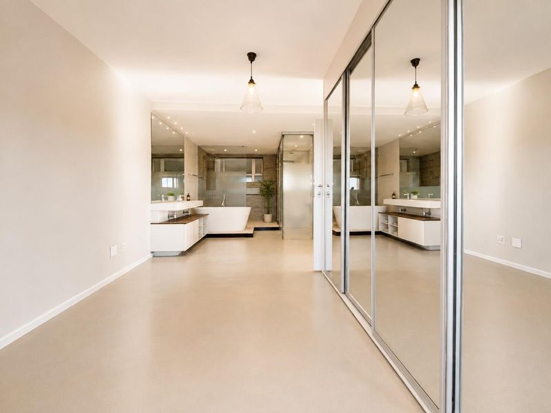 Spacious modern bathroom featuring a freestanding bathtub, walk-in shower, double vanity, and large mirrored sliding wardrobe doors in a clean, minimalist setting.