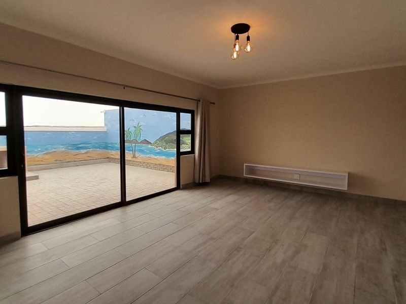 A bright and spacious living room featuring modern tiled flooring, a floating media shelf, and large sliding doors opening onto a patio area.
