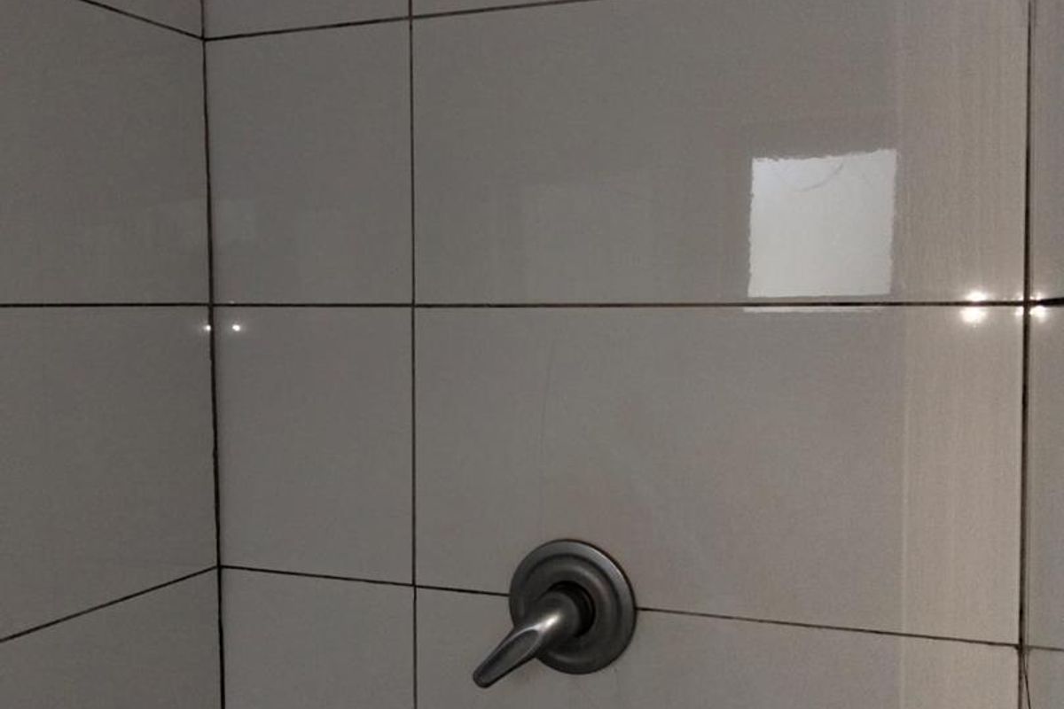 A close-up view of a shower enclosure featuring white ceramic wall tiles, a shower head, and a mixer tap.