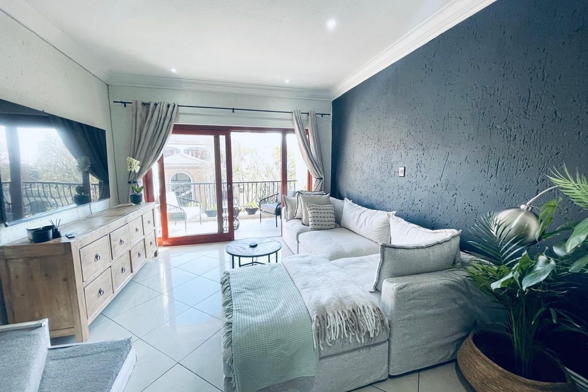 A bright living room featuring polished tiled floors, a textured dark feature wall, and sliding glass doors leading to an outdoor balcony.