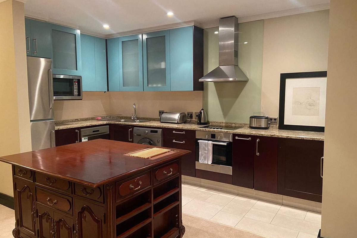 Modern kitchen featuring two-tone cabinetry, granite countertops, stainless steel extractor fan, built-in oven, and integrated appliances.