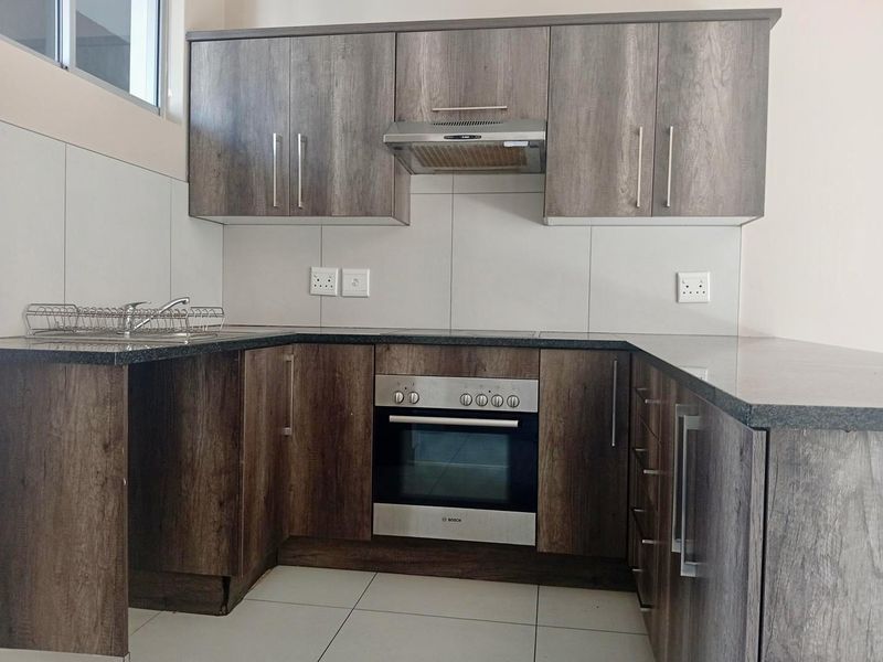Modern kitchen featuring dark wood-grain cabinetry, granite countertops, built-in oven, extractor fan, and tiled splashback in a clean, functional layout.