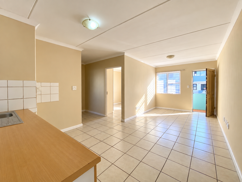 An open-plan living and kitchen area featuring neutral wall tones, tiled flooring, and direct access to an outdoor balcony space.
