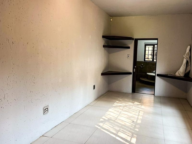 An empty bedroom featuring tiled flooring, built-in corner shelving, and direct access to an adjoining bathroom.