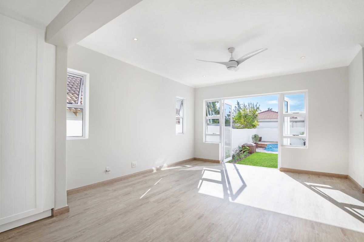 Bright and airy living room featuring light wood-look flooring, recessed lighting, a ceiling fan, and double doors opening to a private garden and pool area.