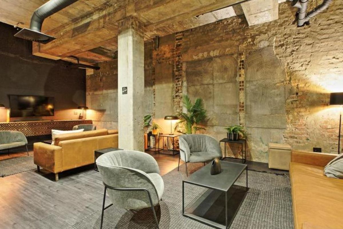 Spacious industrial-style living area featuring exposed brick walls, concrete ceiling beams, and visible ductwork, creating a unique urban aesthetic.