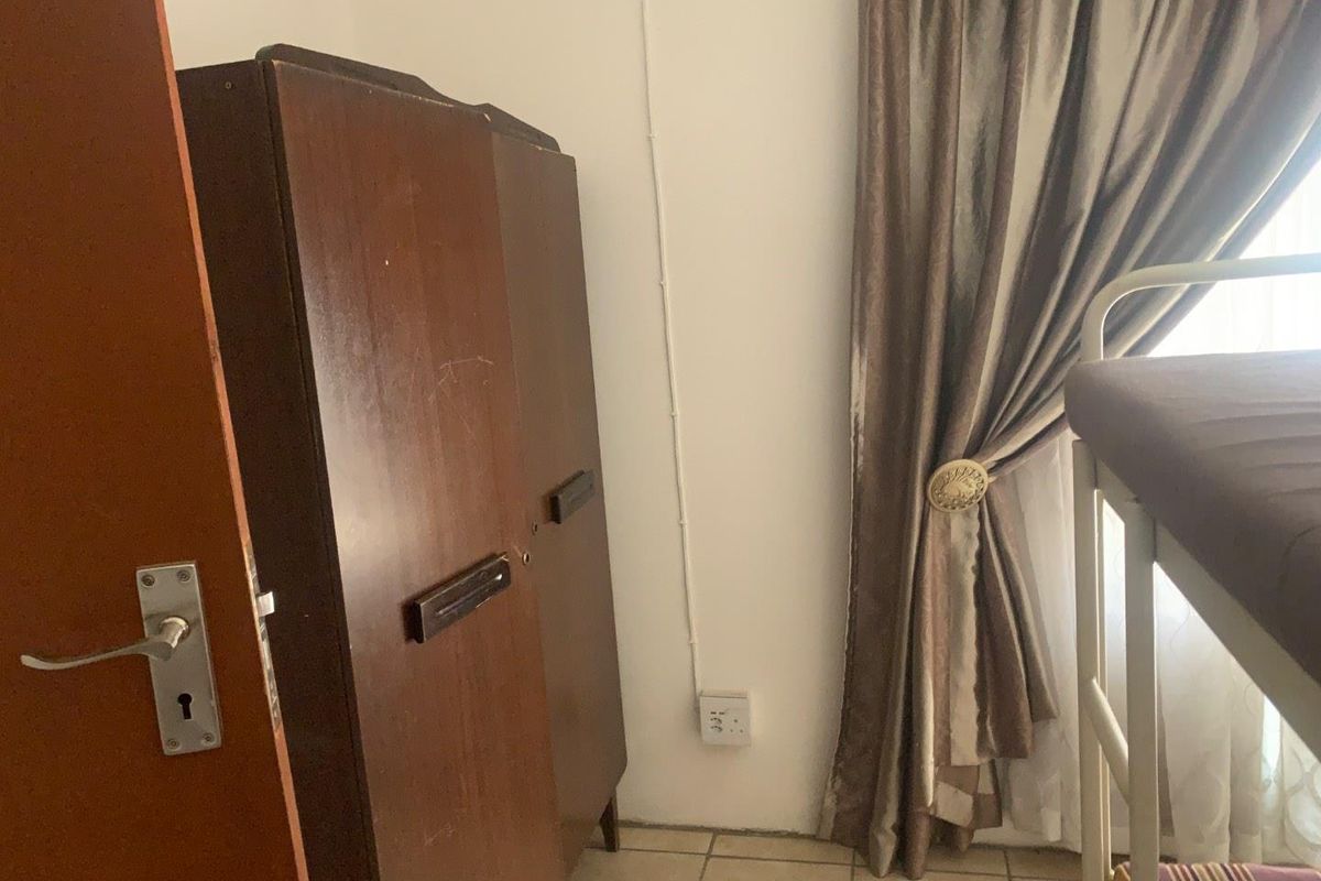 A bedroom featuring tiled flooring, a standard door, and a window with curtain treatments.