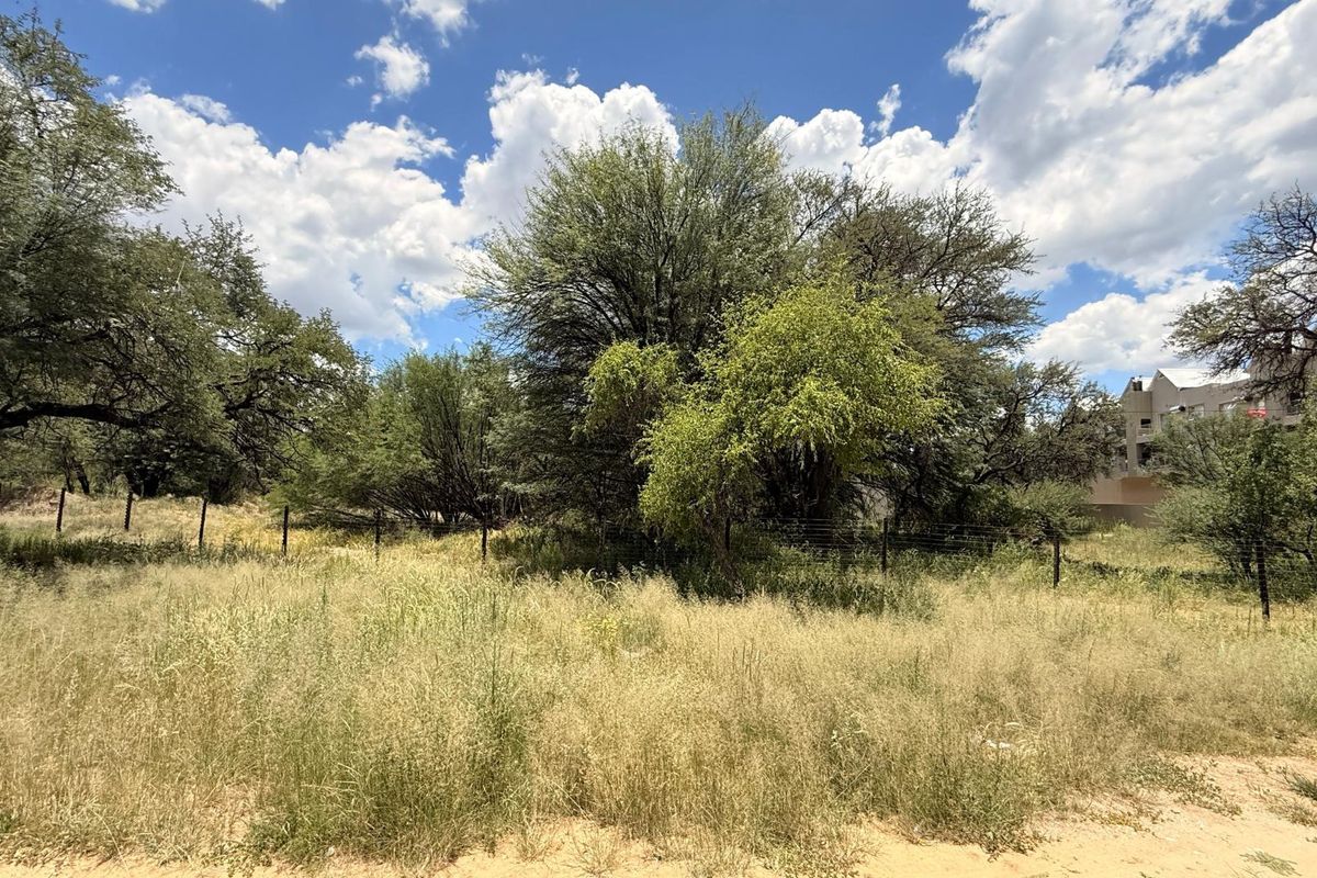 A view of a vacant residential plot featuring mature trees, natural grass cover, and perimeter wire fencing.