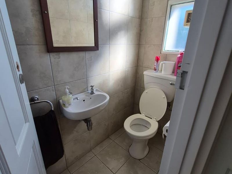A compact guest bathroom featuring tiled walls and flooring, a wall-mounted basin, and a standard toilet.