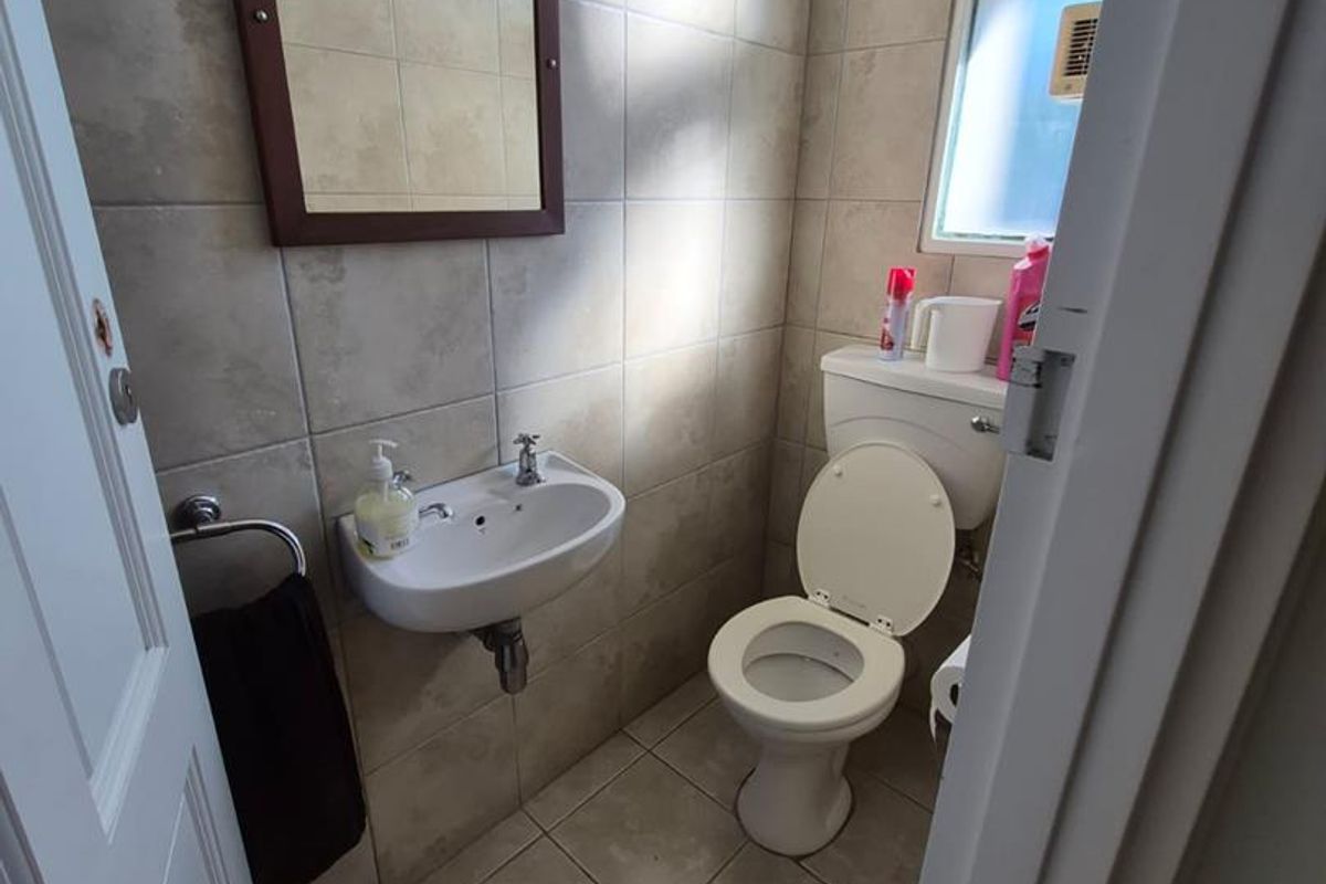 A compact guest bathroom featuring tiled walls and flooring, a wall-mounted basin, and a standard toilet.