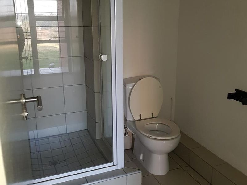A functional bathroom featuring a tiled shower enclosure and a standard toilet, presented in a clean, neutral, and vacant condition.