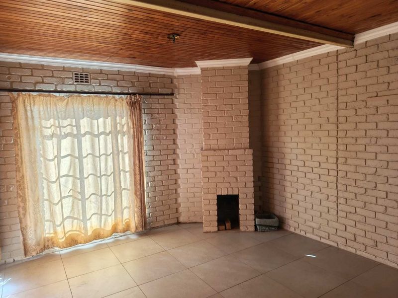 Spacious living room featuring a brick fireplace, timber ceiling, and tiled flooring with access to the outdoors via a sliding glass door.