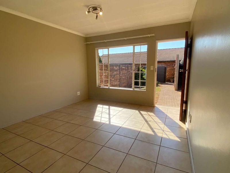 An empty, sunlit living room featuring neutral tiled flooring, a large window, and direct access to the exterior patio area.