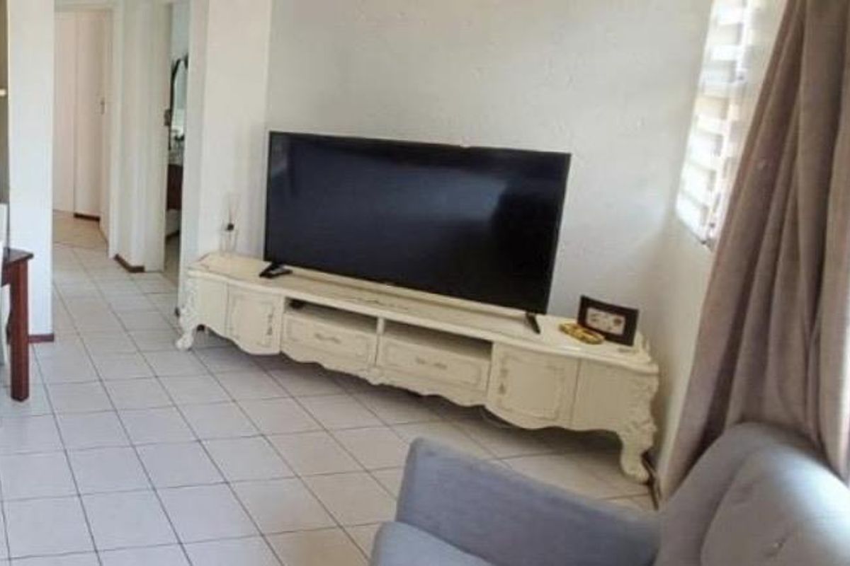 A living room area featuring tiled flooring and a neutral wall finish, providing a functional space with access to adjacent rooms.