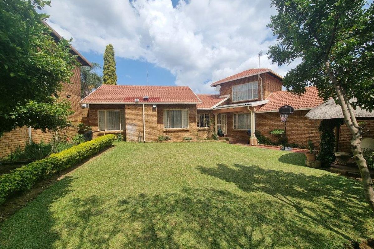 A well-maintained rear garden featuring a spacious lawn, established hedging, and a face brick house exterior with a tiled roof.